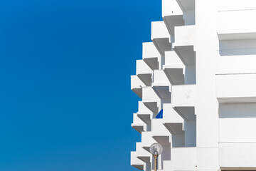 Modern white building facade with geometric balconies against a clear blue sky