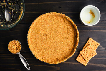 Unbaked Graham Cracker Crust in a Tart Pan: Freshly made graham cracker crumb crust surrounded with kitchen tools and extra ingredients