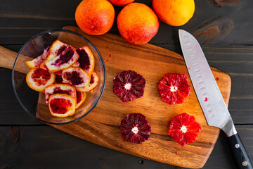 Peeled and Deseeded Blood Oranges on a Wooden Cutting Board: Peeled, halved, and whole raspberry oranges with a chef's knife and peels on the side
