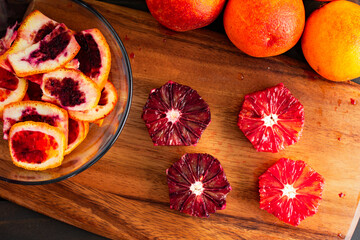 Peeled and Deseeded Blood Oranges on a Wooden Cutting Board: Peeled, halved, and whole raspberry oranges with peels on the side viewed from above