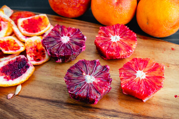 Peeled and Deseeded Blood Oranges on a Wooden Cutting Board: Peeled, halved, and whole raspberry oranges with peels on the side viewed from above