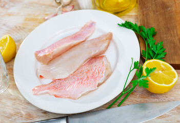 Raw fish with condiments, red perch fillet on plate with garlic and parsley on wooden surface