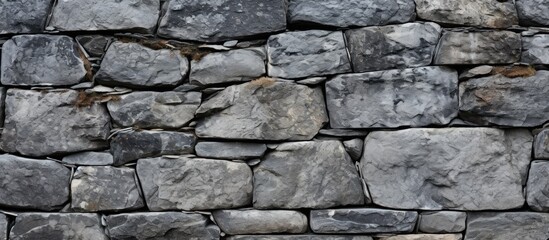 Fototapeta premium A close up of a grey stone wall constructed with large rectangular rocks, showcasing a beautiful pattern of bedrock building material resembling flagstone brickwork, perfect for flooring