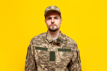 serious Ukrainian army soldier in pixel camouflage uniform on yellow isolated background, Ukrainian...