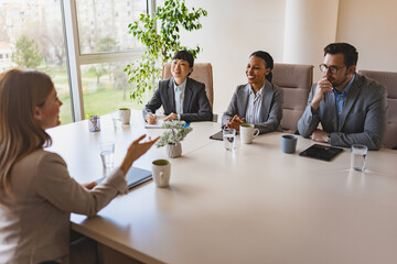 A diverse group of multi-ethnic businesswomen sit in a corporate office and have a meeting with a business associate - obrazy, fototapety, plakaty