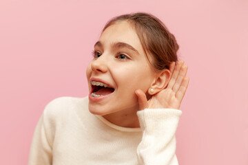 curious teenage girl with braces eavesdrops on secret information on a pink isolated background,...
