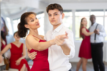 Obraz premium Pretty young woman dancing waltz with partner at group of multinational people in modern ballroom dancing class
