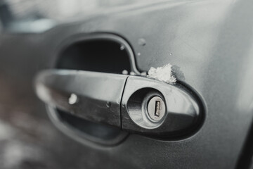 Gray passenger car during a snowy winter, snowy door lock (selective focus)