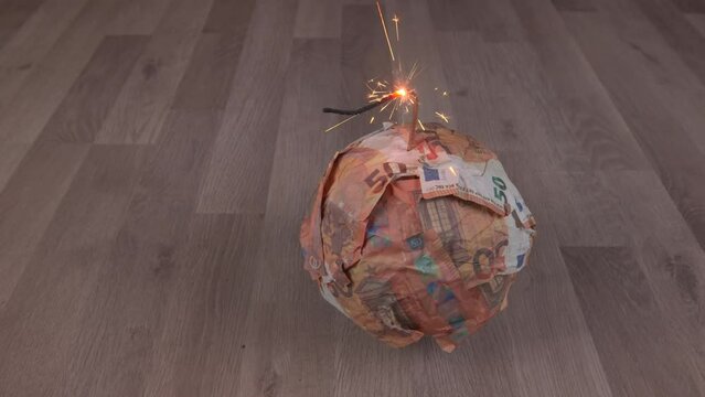 Bomb from Euro banknotes with a burning wick, on a wooden floor. The concept of financial crisis, loss of money, bankruptcy