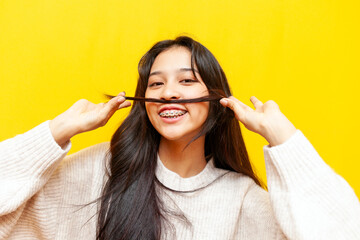 young funny asian woman with braces showing hair mustache on yellow isolated background, korean girl fooling around and making faces and having fun on camera