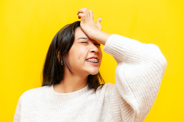 young dissatisfied asian woman with braces shows facepalm on yellow isolated background, korean...