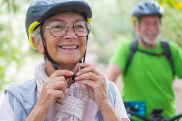 Portrait of one old woman smiling and enjoying nature outdoors riding bike with her husband laughing. Headshot of mature female with glasses feeling healthy. Senior putting on helmet to go trip  - Powered by Adobe