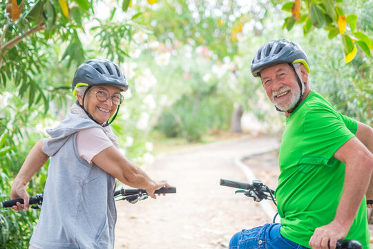 Two happy old mature people enjoying and riding bikes together to be fit and healthy outdoors. Active seniors having fun training in nature. Portrait of two senior looking at the back looking