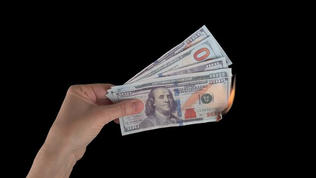 Female hand holding dollar banknotes while burning. Green screen, isolated on black background with alpha channel. The concept of inflation and devolution, the depreciation of money, the global crisis