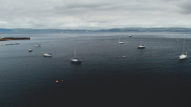 Scotland's ocean aerial view: yachts, ships, boats in summer cloudy day. Seascape of bay of Island Arran, United Kingdom. Beautiful nature landscape. Footage Drone Shot in 4K (UHD).