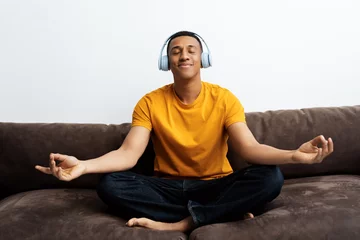  African American man wearing wireless headphones, listening music, in lotus position, meditating © Maria Vitkovska