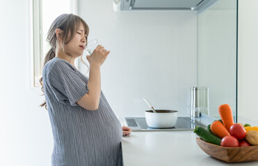 キッチンで水を飲む妊娠後期の妊婦の女性（体調不良・水分補給・悪阻）
