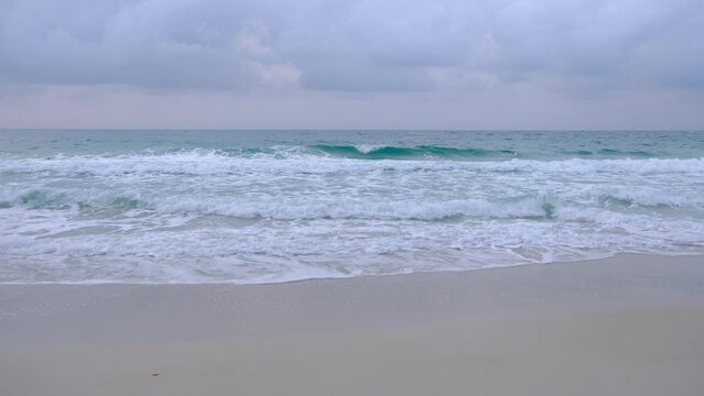 Tiny ocean waves were hitting the sandy beach, creating white foam.