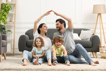 Family housing concept. Happy woman and her husband forming roof with their hands while sitting with kids on floor at home