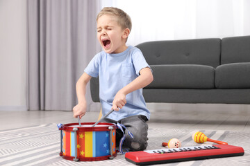 Little boy playing toy drum at home