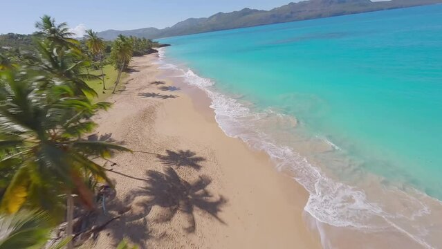 Epic FPV drone flight over palms onto picturesque sandy beach and blue ocean