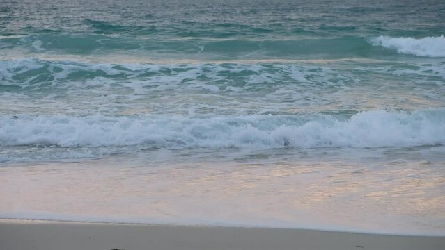 Ocean waves roll onto the sand creating foamy water in the morning.