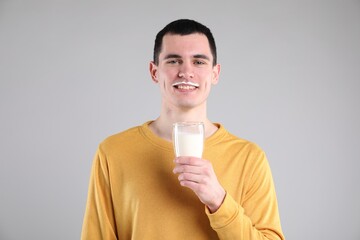 Happy man with milk mustache holding glass of tasty dairy drink on gray background