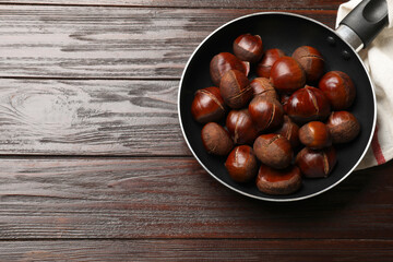 Obraz premium Roasted edible sweet chestnuts in frying pan on wooden table, top view. Space for text