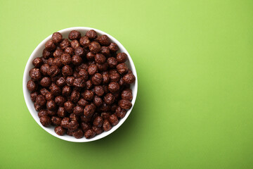 Chocolate cereal balls in bowl on green table, top view. Space for text