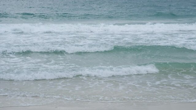 Closeup blue waves crashing on the brown sandy beach.