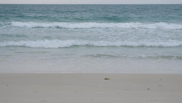 Ocean waves roll onto the brown sand beach.