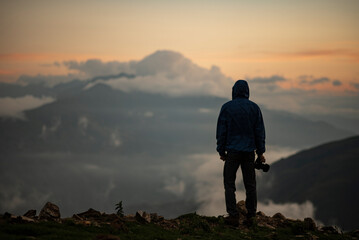 silhouette of a person on a mountain top taking photos holding a camera.