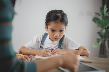 A young girl is sitting at a table writing in a notebook