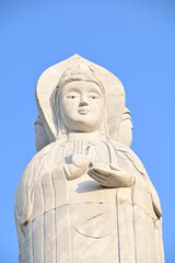 Obraz premium Closeup of The White Guan Yin Statue is the Bodhisattva of Mahayana Buddhism standing in a beautiful Thai Buddhist temple at Thailand with blue sky background.