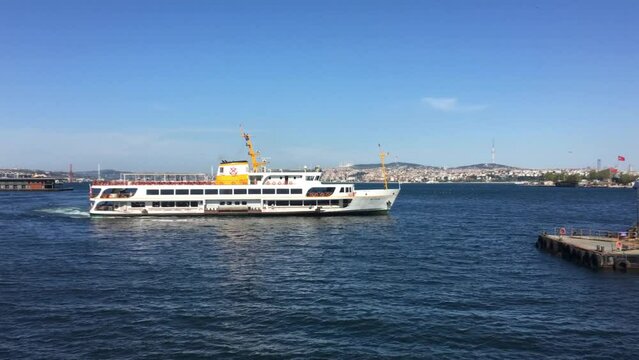 A ferry leaves port across the Bosporus in Istanbul Turkey. The weather is beautiful, the sun is bright. the large ship carrying people moves along the iconic skyline and towards the Asian side. 