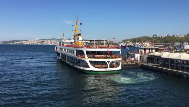 A ferry transporting people across the Bosporus leaves port in Istanbul Turkey. The weather is beautiful, the sun is bright. 