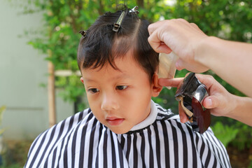 Portrait of Asian boy cut in hairdresser's machine in the garden - 761950974