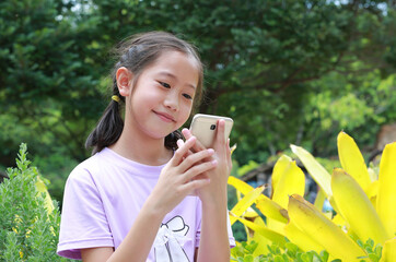 Smiling Asian girl kid using smartphone while in park outdoor. Distant communication concept. - 761951311