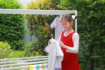 Portrait of happy Asian girl hanging the laundry on a clothes rail with looking camera at garden near house. - 761951583