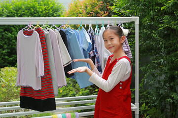 Asian girl child helping to do dry the clothes at the garden near house. Kid hanging cloth on a clothesline. - 761951747
