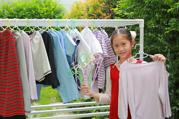 Portrait of happy Asian girl hanging the laundry on a clothes rail with looking camera at garden...