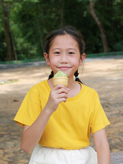 Smiling Asian young girl child eating tasty green tea ice cream in the garden. - 761951999