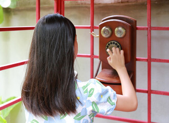 Rear view of Asian young girl kid using dial telephone booth. Child call on the retro vintage red phone booth. - 761952131