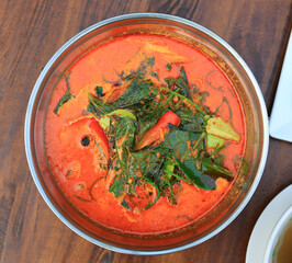 Periwinkle curry with cha plu leaf in aluminium bowl on wood table background. Delicious hot and spicy Thai food. Top view. - 761952793