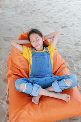 Portrait of Asian young girl in dungarees jean relax and sleeping on orange sofa bed beach on sand at summer holiday. - 761953189