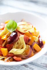 Tagliatelle pasta with pepper, red onion and basil. Bright wooden background