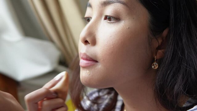 Close up portrait of beautiful young Asian woman applying make up using make up brush and puff, getting ready to hang out. Beauty tips, beauty vlogger concept