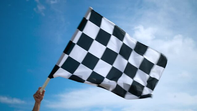 A developing checkered racing flag made of wavy silk fabric in the hand of a man against the sky.