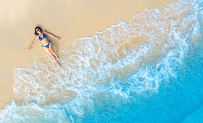 Aerial view of beautiful young woman in blue bikini lying on sandy beach near blue sea with waves at sunset Summer vacation at Andaman Island