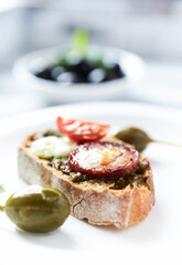 Crostini with tomato, salami and olive pesto on wooden background.
